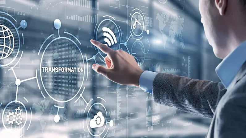 Hand einer Person in Hemdärmel, die auf ein digitales Display mit dem Wort 'TRANSFORMATION' und vernetzten Symbolen zeigt