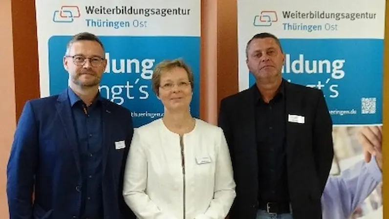 Drei Personen stehen vor zwei Bannern der Weiterbildungsagentur Thüringen Ost