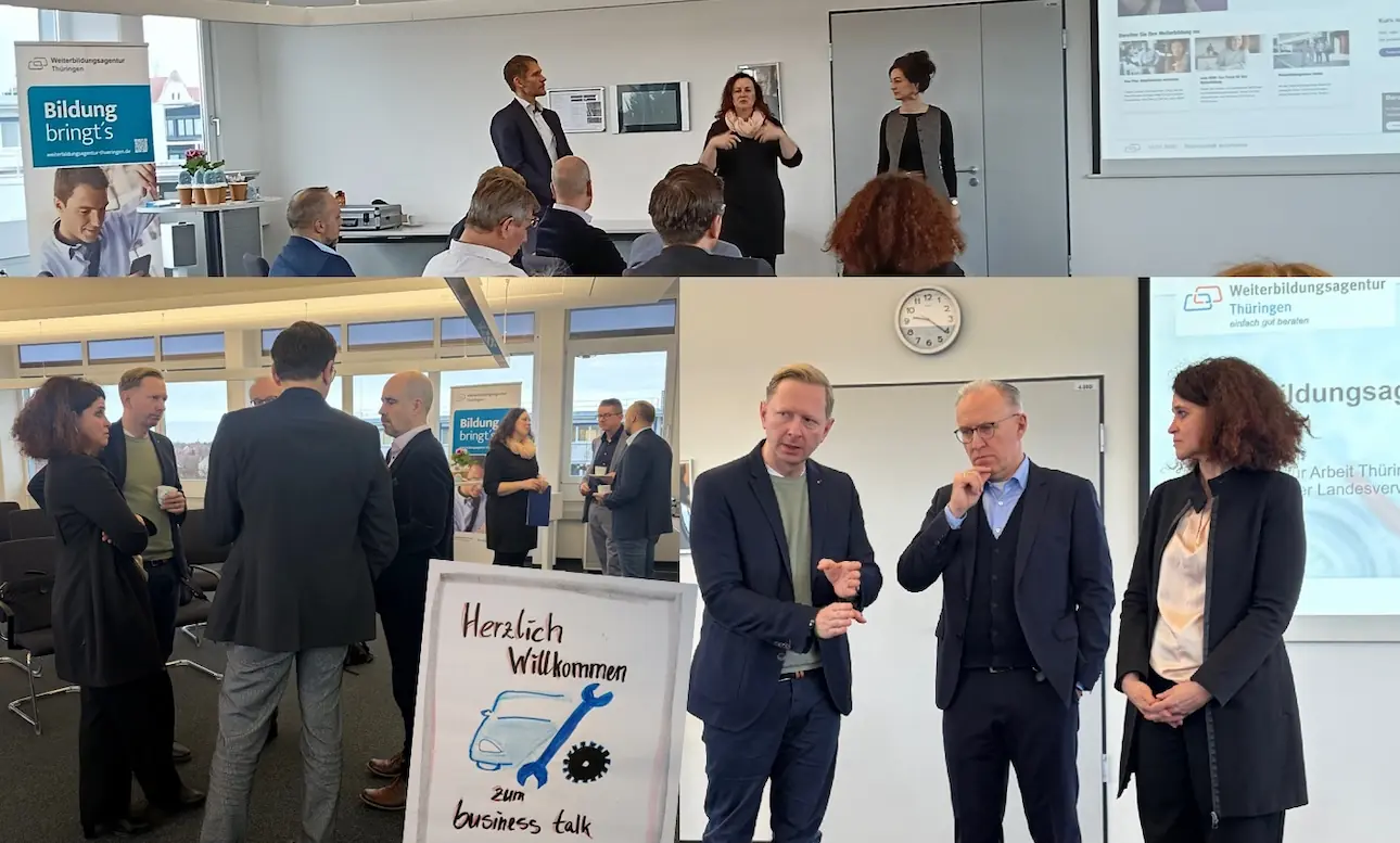 Mehrere Personen stehen und sitzen in einem Seminarraum, einige sprechen vor einer Leinwand, andere unterhalten sich in kleinen Gruppen, im Vordergrund ein Schild mit der Aufschrift 'Herzlich Willkommen zum business talk'.