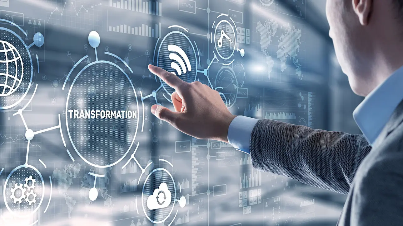 Hand einer Person in Hemdärmel, die auf ein digitales Display mit dem Wort 'TRANSFORMATION' und vernetzten Symbolen zeigt