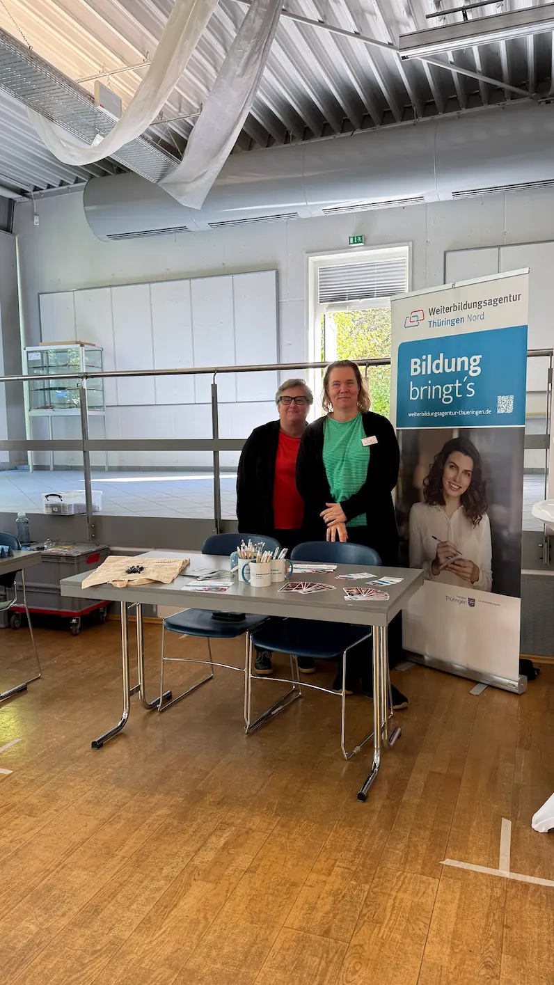 Yvonne Werther und Claudia Brauer-Henze stehen hinter dem Messestand der Weiterbildungsagentur Thüringen Nord auf der BBK.