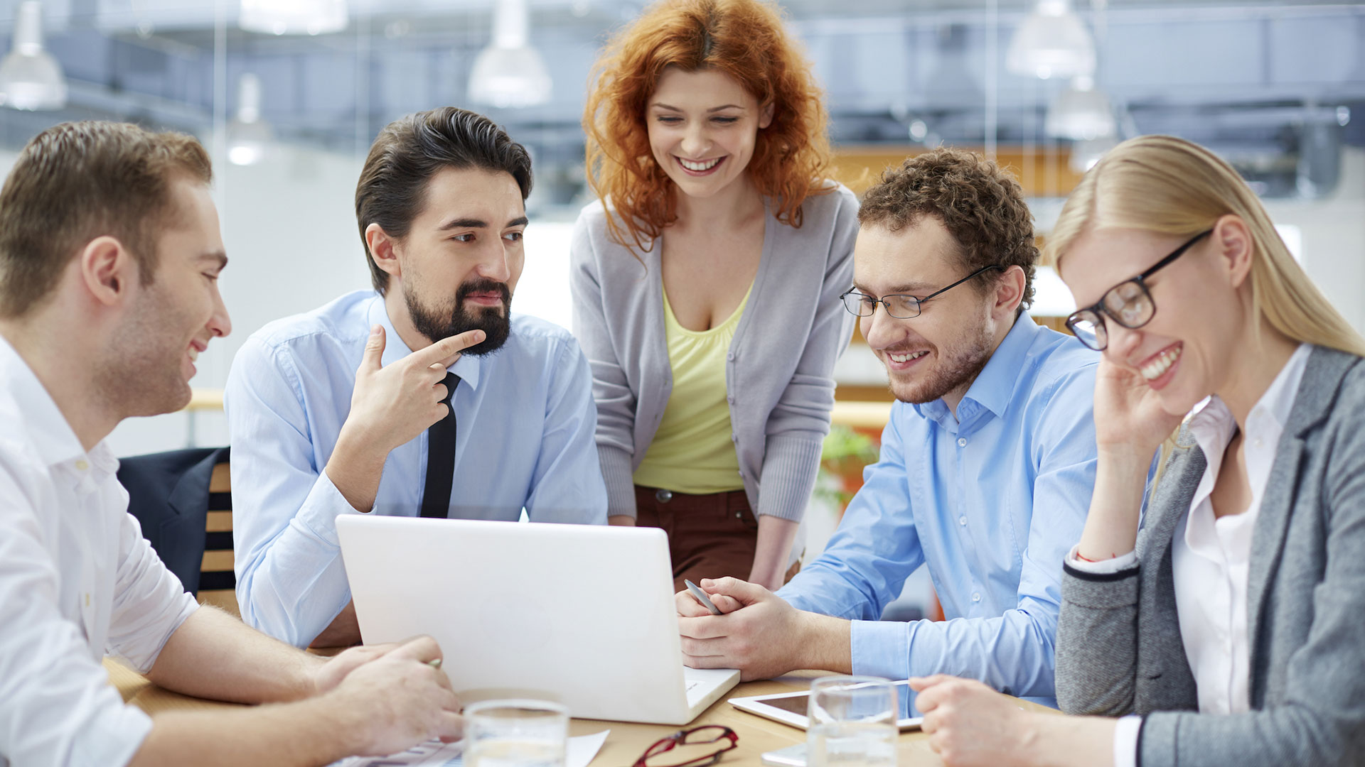 Fünf Personen sitzen um einen Tisch mit Laptop und Tablets, diskutieren in einem modernen Büro, Thema Weiterbildung.