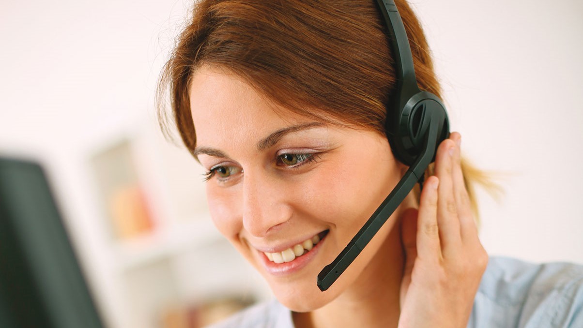 Frau mit Headset spricht, während sie am Computer sitzt. Kontext: Telefonberatung zu Weiterbildung.